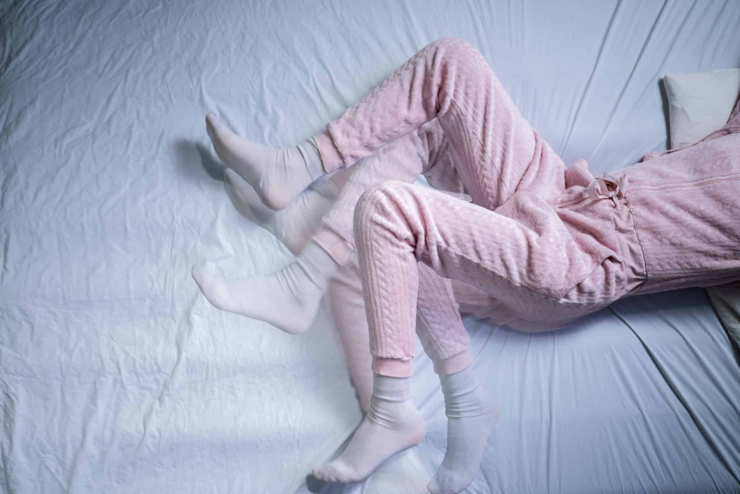 Woman, wearing pink pajamas, struggles with restless legs